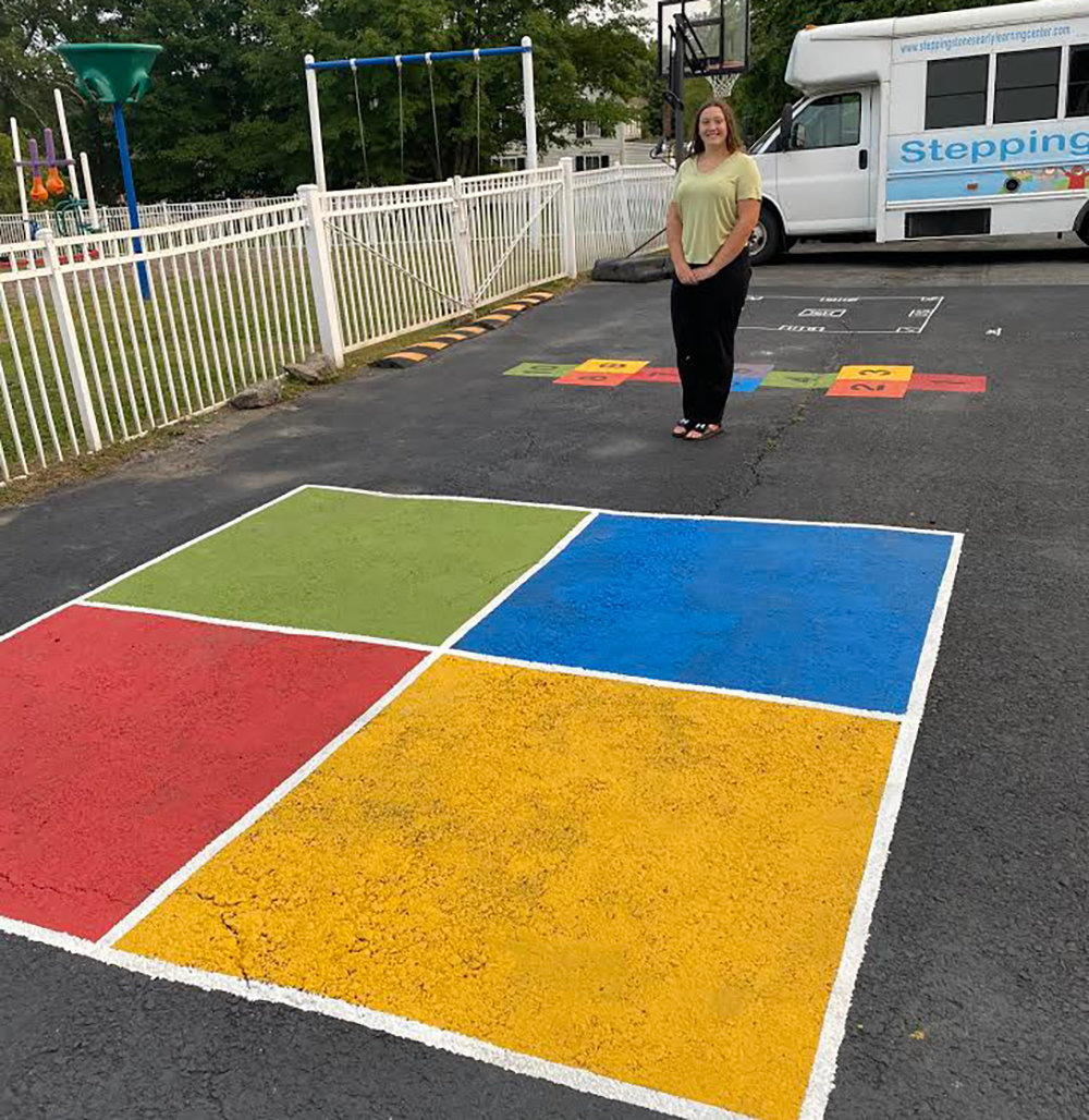 Girl Scout Abigail Gaer stands beside her four square game space, one of several that she created at the Stepping Stones Early Learning Center in Milton to earn her Silver Award in scouting.